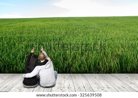 Two people from the rear sitting on the wooden floor shows hands