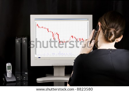 Businesswoman at her workplace. Business graph\'s going down on computer monitor