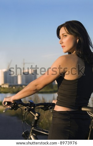 Woman on bike is having rest at sunset light. Urban scene on background.