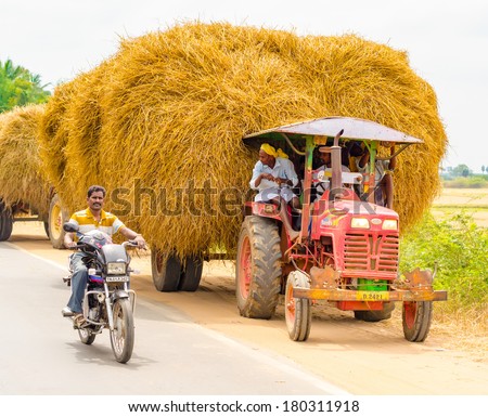 THANJAVOUR, INDIA - FEBRUARY 13: Unidentified indian rural men stopped at the curb on a car with straw and a man riding a motorcycle on the road.  India, Tamil Nadu, near Thanjavour. February 13, 2013