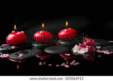 spa concept of white and red orchid (cambria), three  red candles and pearl beads on zen stones with drops, reflection water