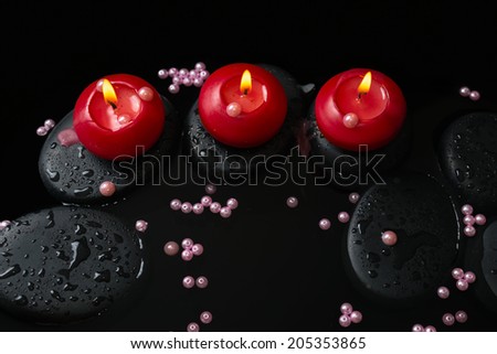 Beautiful spa still life of candles, zen stones with drops and pearl beads on reflection water