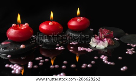 spa setting of red candles, orchid cambria flower on zen stones with drops and pearl beads in reflection water
