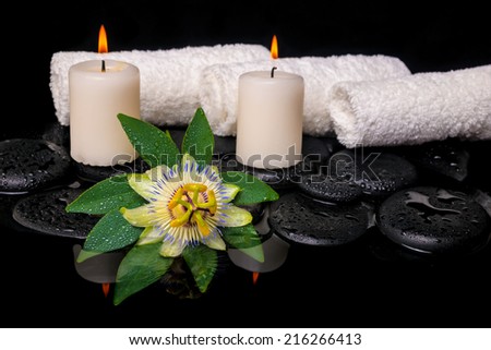 spa still life of passiflora flower, green leaf with drop, towels and candles on zen stones in reflection water