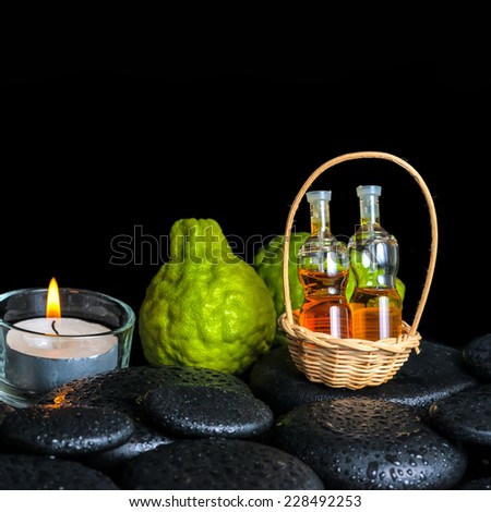 Aromatic spa concept of bergamot fruits, candle and bottles essential oil in basket on zen black stones with dew, closeup