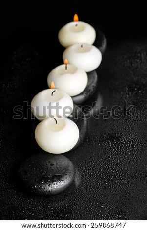 spa concept of candles on zen stones with water drops on black background