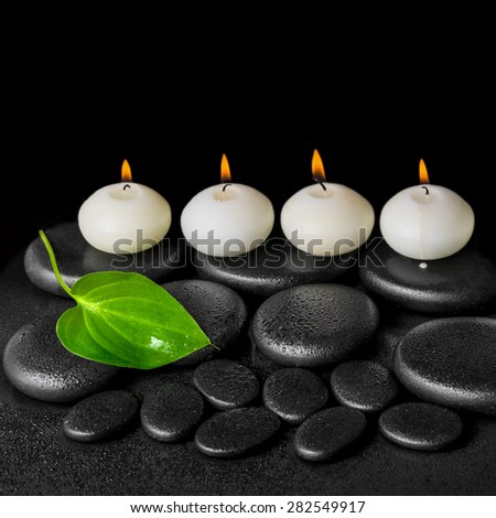 spa concept of white candles and green leaf on black zen stones background with dew, closeup