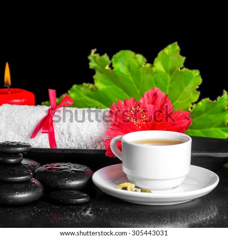 beautiful spa concept of red hibiscus flower with dew, candles, green leaf, cup of tea and rolled towel on zen stones, closeup