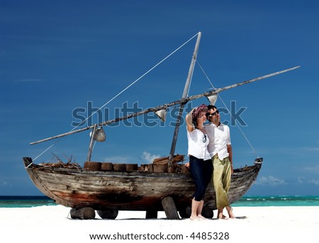 Young happy couple posing near old ship at tropical white sand beach
