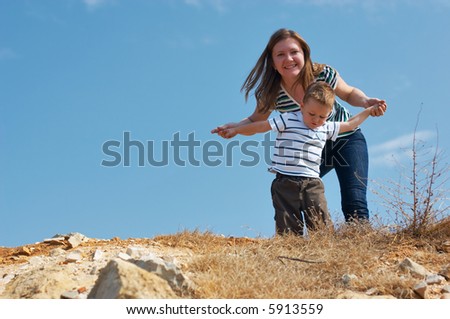 We can fly. Mother and son playing outdoors on top of hill at sunny day