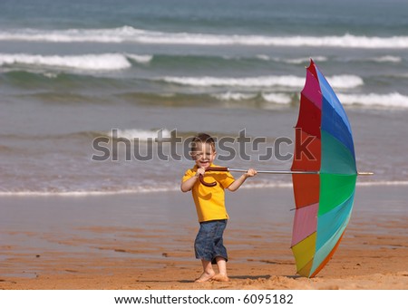 Don’t depend on weather conditions. Cute small boy with big brightly colored umbrella having fun on the beach.