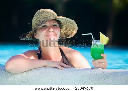 Girl relaxing in swimming pool with glass of tropical drink
