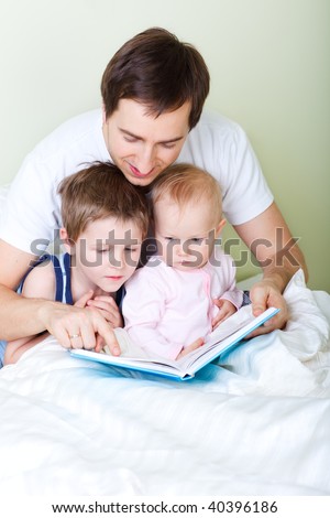 Young father and two kids reading book in bed