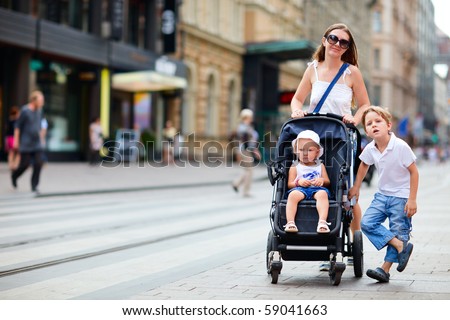 Young mother with her son and toddler daughter in stroller walking in city center