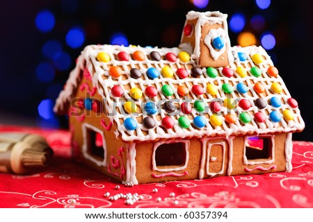 Gingerbread house decorated with colorful candies over Christmas tree lights background