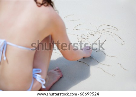 Young woman in white bikini drawing tropical island on white sand