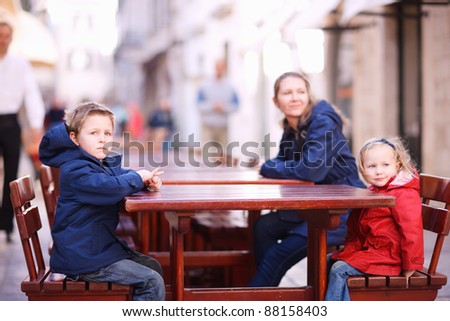 Mother and two kids relaxing at empty street restaurant on autumn day
