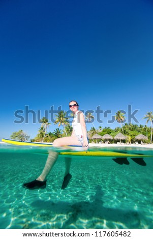 Woman sitting on a surfboard at ocean in front of tropical island