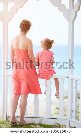 Back view of mother and daughter enjoying sea view