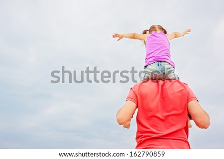 Back view of father carrying his little daughter on shoulders