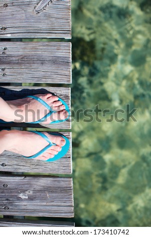 Woman legs wearing flip flops at wooden jetty by the sea