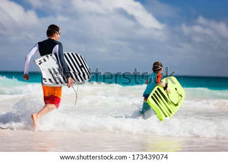Father and son running towards ocean with boogie boards