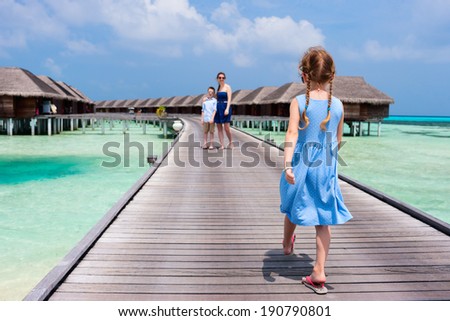 Back view of a little girl walking toward her family on wooden jetty at resort