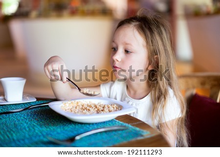Adorable little girl eating cereal with a milk for a breakfast in restaurant