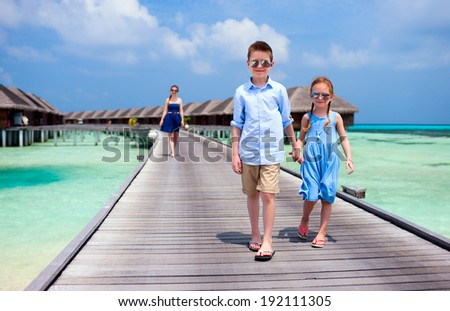 Cute little kids walking together on wooden jetty at tropical resort