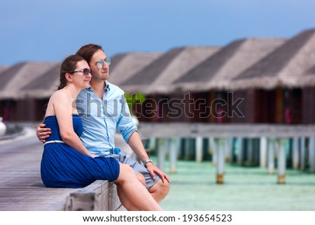 Romantic couple sitting on wooden jetty in front of over the water villas on a tropical beach during  vacation