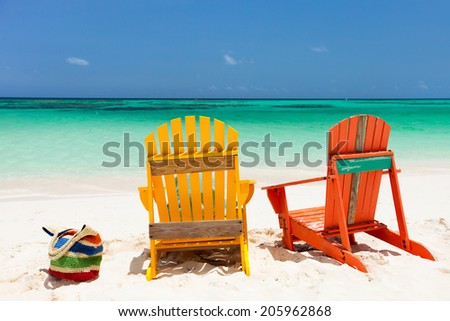 Colorful yellow and orange lounge chairs at tropical beach in Caribbean with beautiful turquoise ocean water, white sand and blue sky
