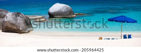 Panorama of a picture perfect beach with blue umbrella, white sand and turquoise ocean water at tropical island in Caribbean