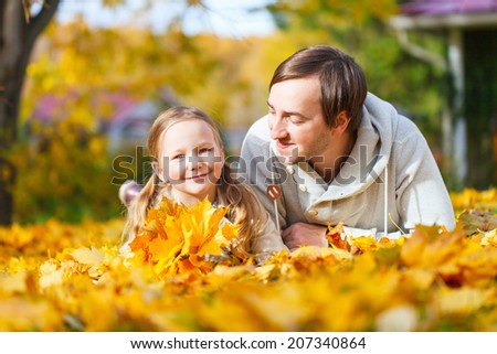 Father and his adorable little daughter outdoors on sunny autumn day laying on ground covered with fallen yellow leaves