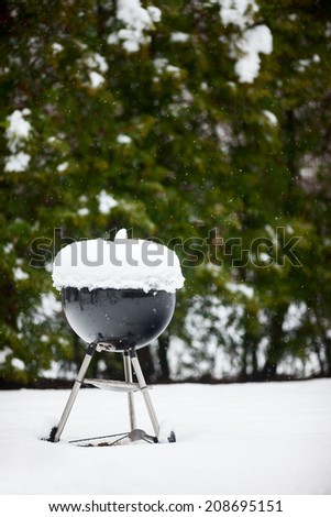 Black barbeque grill covered with snow outdoors on winter day