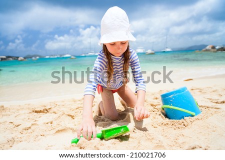 Adorable little girl wearing sun protection rash guard at beach during summer vacation