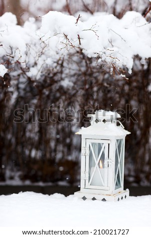White Christmas decoration lantern with candle on snow ground at winter day
