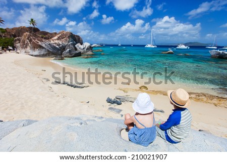 Back view of two kids sitting on granite boulder and enjoying beautiful scenery of The Baths beach area major tourist attraction at Virgin Gorda, British Virgin Islands, Caribbean