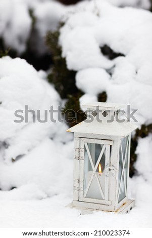 White Christmas decoration lantern with candle on snow ground at winter day