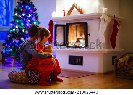 Two little kids sitting by a fireplace at home on Christmas eve