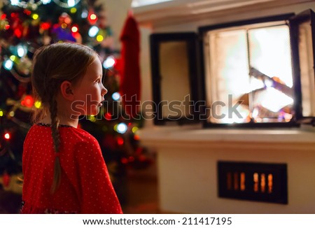 Adorable little girl sitting by a fireplace at cozy family home on winter