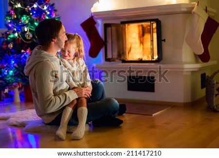 Father and daughter sitting by a fireplace in their warm family home enjoying winter evening