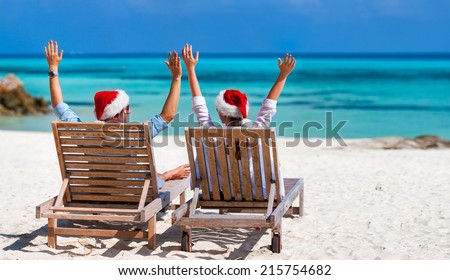 Back view of a happy couple in Santa hats relaxing on a tropical beach during Christmas vacation, panorama perfect for banners