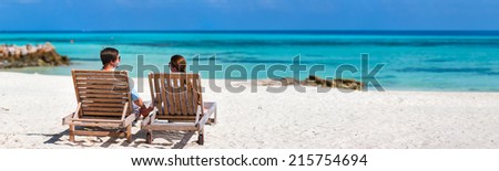 Back view of a couple relaxing on a tropical beach during summer vacation, panorama perfect for banners