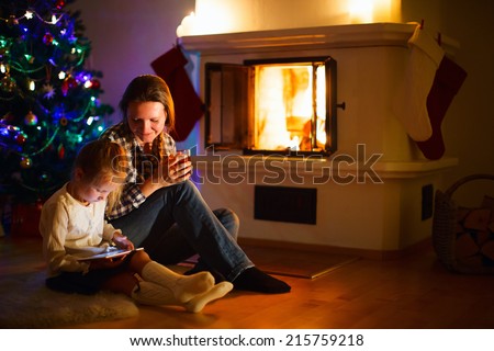 Mother and daughter sitting by a fireplace in their family home on winter