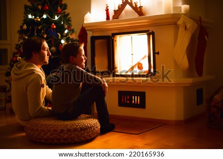 Father and his son sitting by a fireplace in their family home on Christmas eve