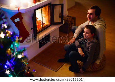 Father and his son sitting by a fireplace in their family home on Christmas eve