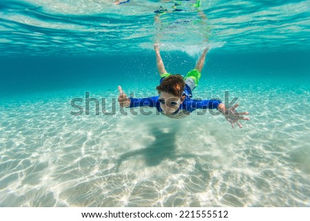 Cute teenage boy swimming underwater in shallow turquoise water at tropical beach