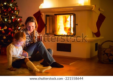 Mother and daughter sitting by a fireplace in their family home on winter
