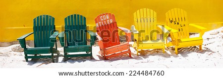 Row of colorful wooden chairs at tropical white sand beach in Caribbean against colorful wall