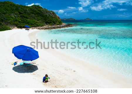 Kids playing on picture perfect beach with blue umbrella, white sand, turquoise ocean water and blue sky at tropical island in Caribbean